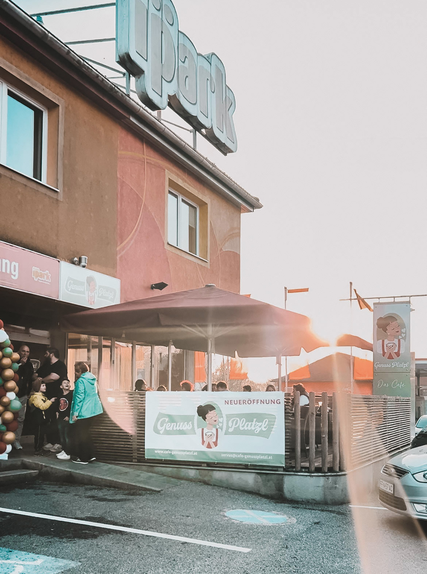 Außenansicht des glutenfreien Café Genussplatzl in Ilz mit Schild, Werbebanner und Menschen vor dem Eingang.
