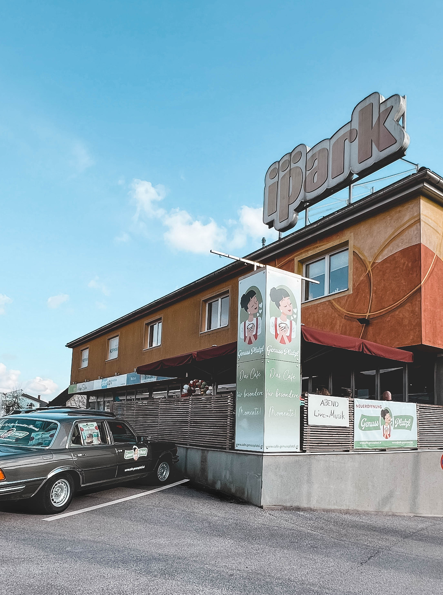 Glutenfreies Café Genussplatzl Ilz mit Werbung an der Fassade des ipark Gebäudes mit einem Oldtimer im Vordergrund