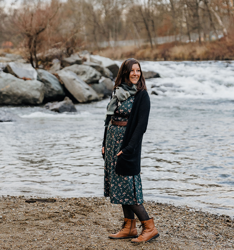 Verena, Grafikdesignerin und Gründerin von farbgefühl, steht lächelnd an einem Fluss in der Natur - Grafikdesign Agentur in Leibnitz