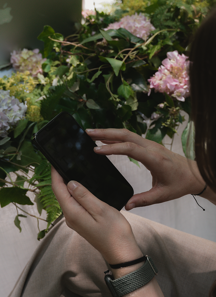 Hände bedienen Smartphone im Blumenarrangement